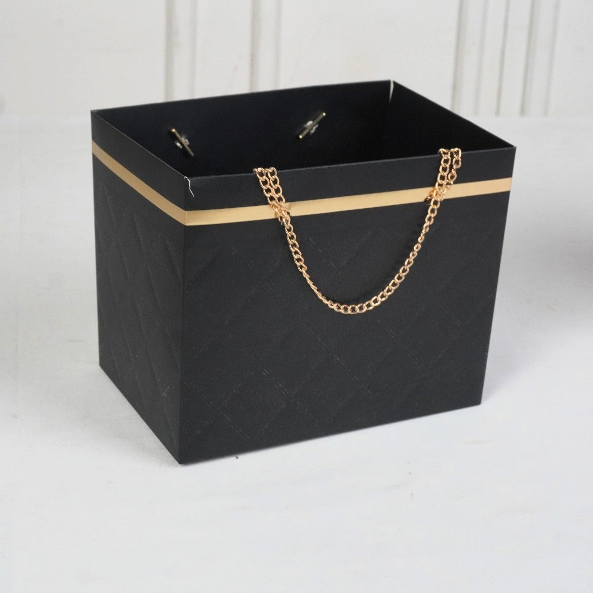 Black paper bag with gold chain handle on a white background