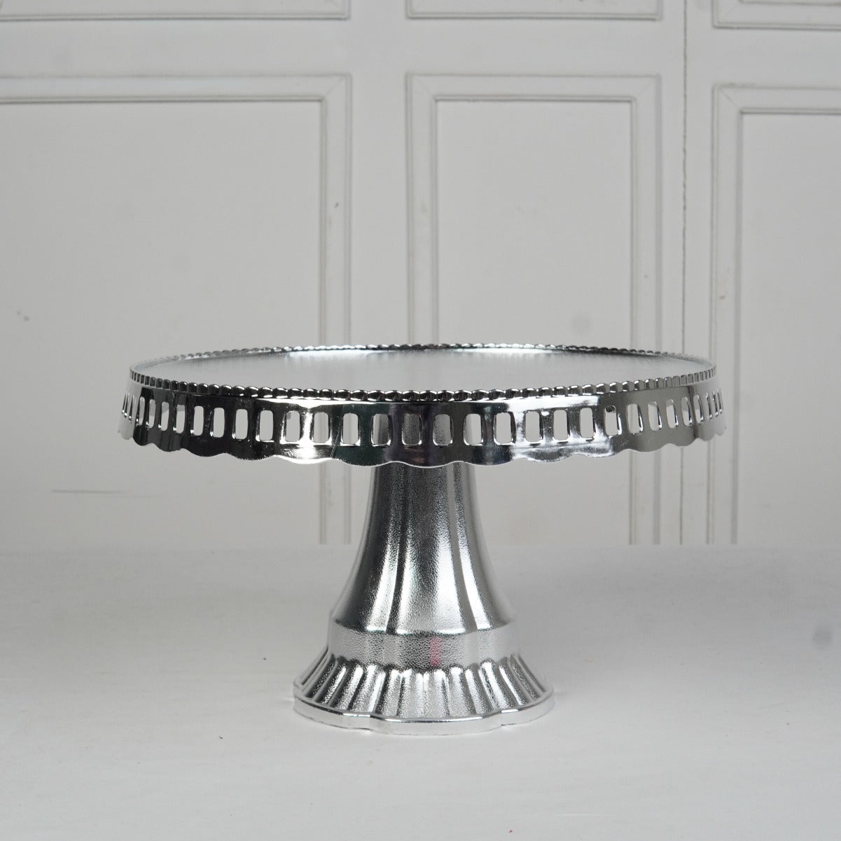 Silver cake stand on a white surface with a white paneled background